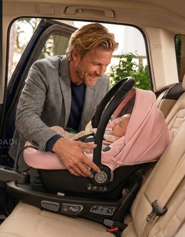 Szczęśliwy tata z łatwością wpina różowe nosidełko Avionaut na bazę ISOFIX w samochodzie, co ilustruje wygodę, szybkość i bezpieczeństwo tego rozwiązania